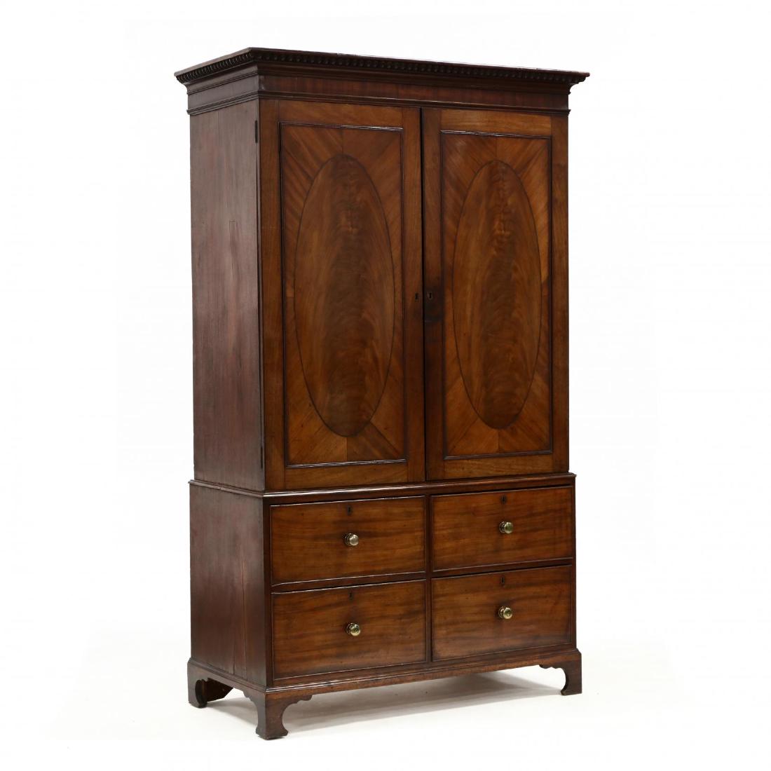 George III Mahogany Linen Press: George III Mahogany Linen Press circa 1800, two part form, gadrooned and cove molded cornice over two hinged doors having oval inlaid panels, interior with fitted drawers and later metal electronic pl
