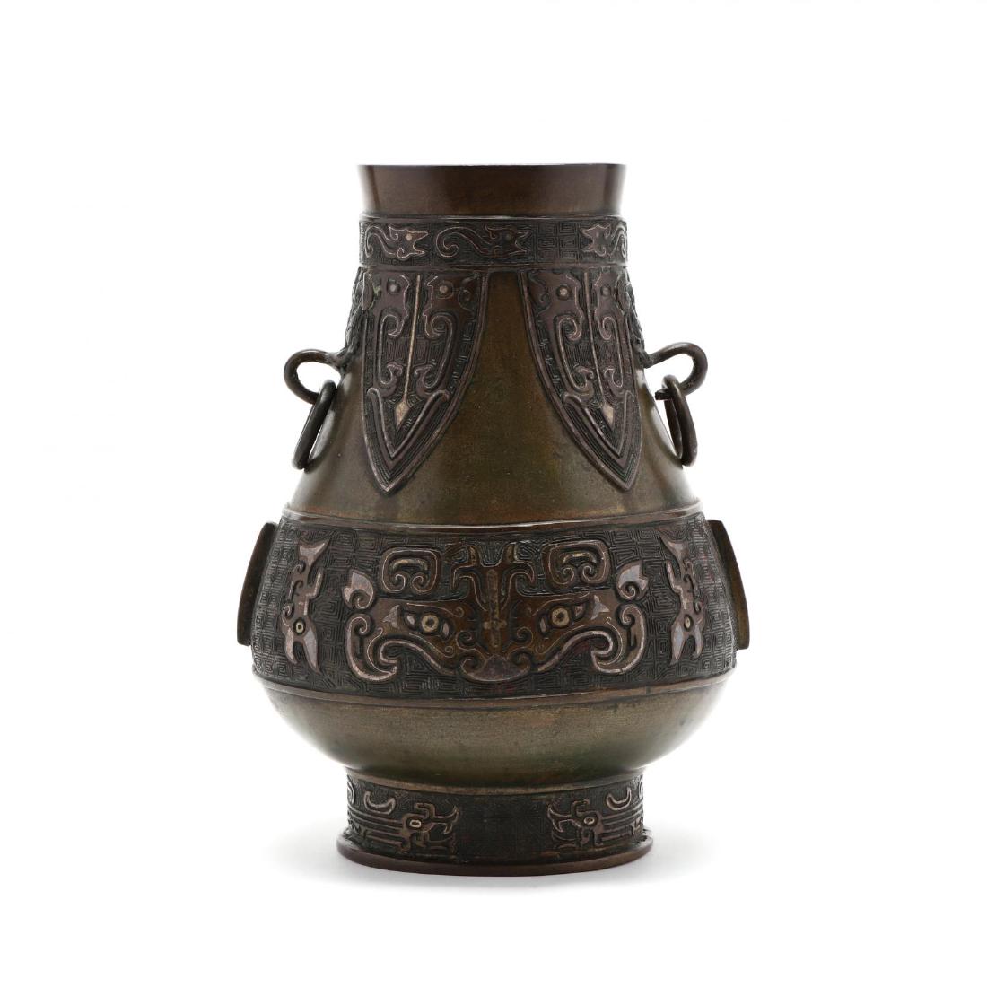 A Chinese Archaic Hu Style Bronze Vessel: A Chinese Archaic Hu Style Bronze Vessel hu shaped wine vessel flanked with two masked face handles with rings, decorated with key motif and geometric lappets around neck and thick band with taotie ma