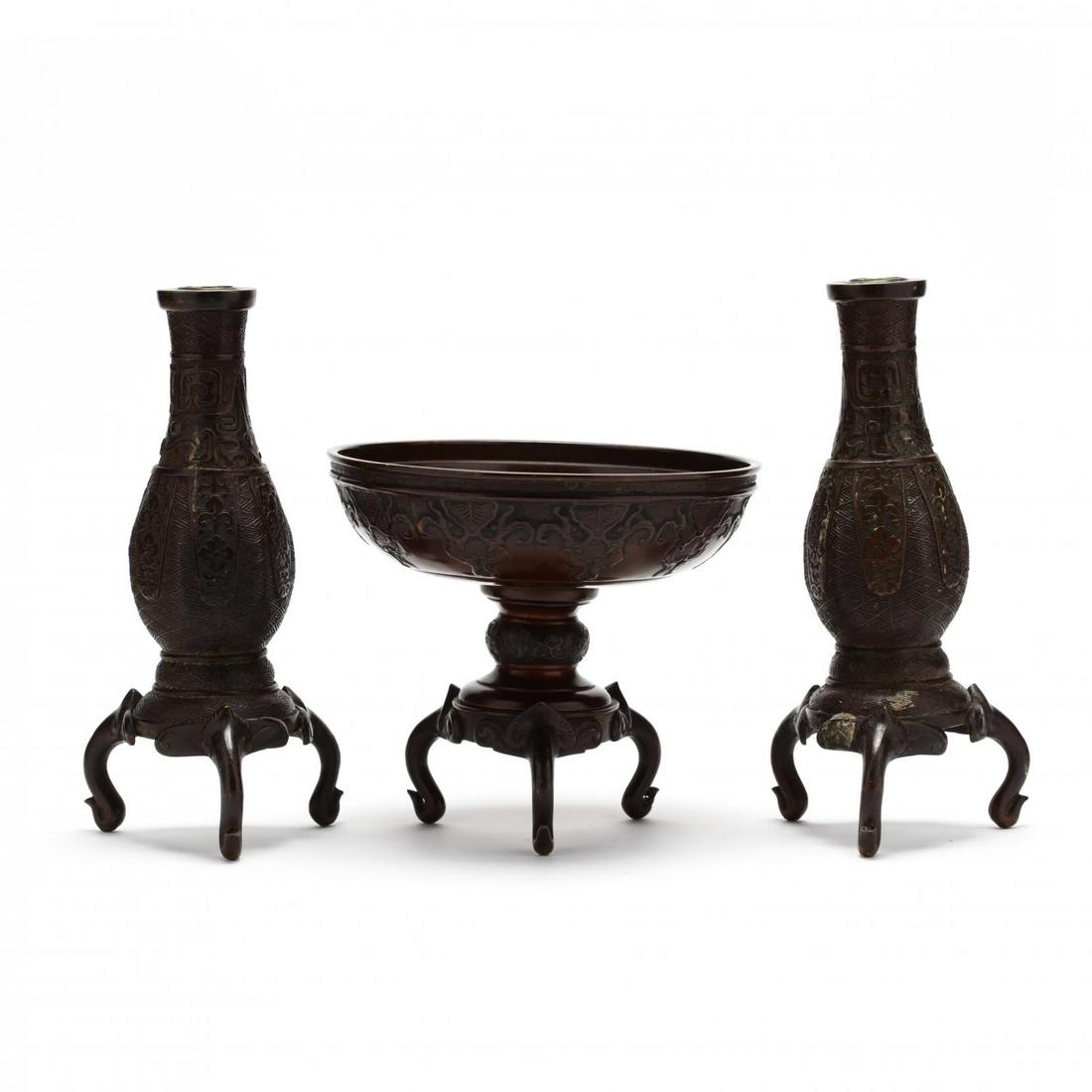 A Japanese Bronze Group of Table Accessories: A Japanese Bronze Group of Table Accessories first half of 20th century, includes a pair of bronze candlesticks in archaic style raised on three elephant head legs, and a bronze Japanese tazza often u
