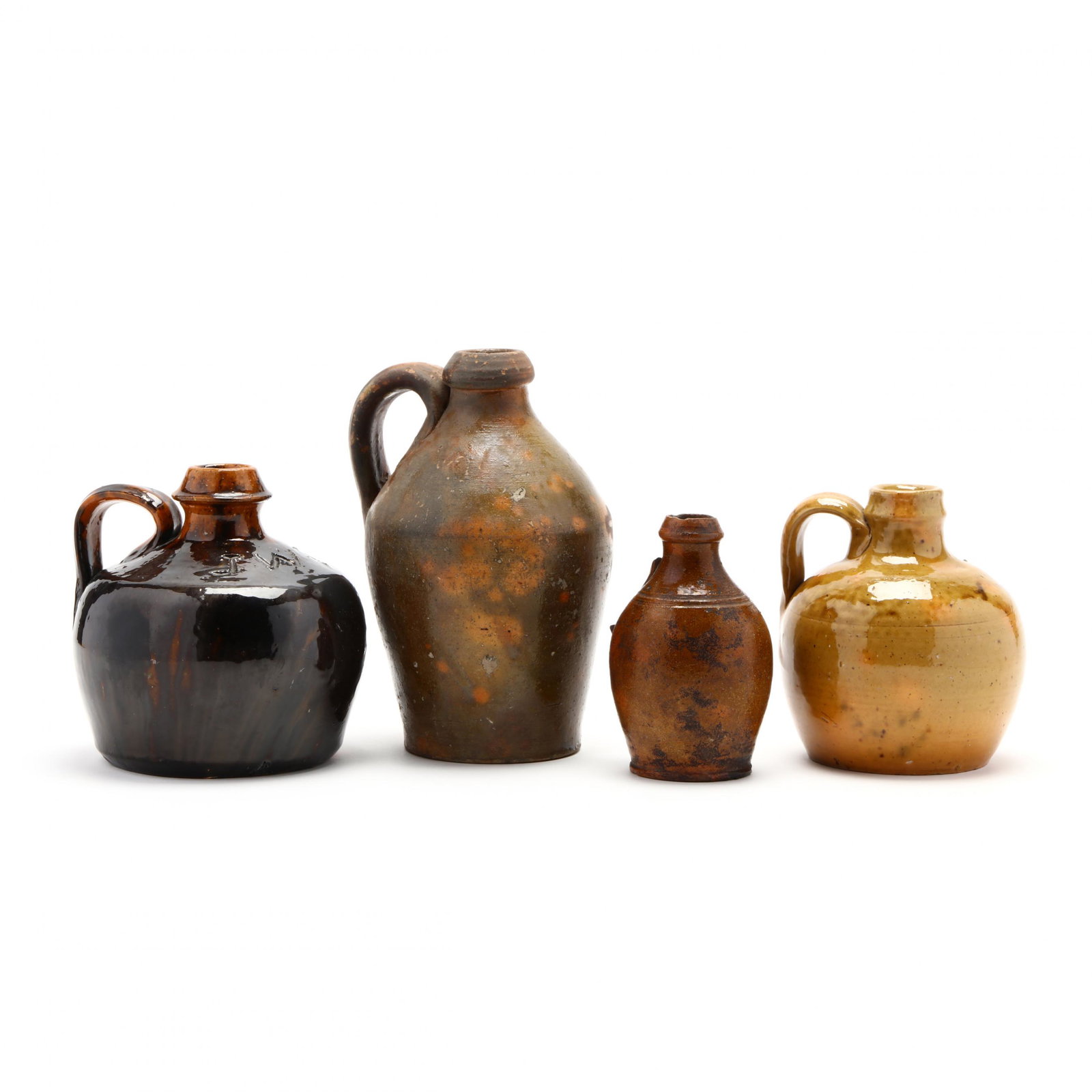 NC Pottery, Four Jugs: NC Pottery, Four Jugs an earthenware jug with 'mistake' glaze (8 in.) (glaze losses); a clear glazed low jug; an early Randolph County miniature jug with incised bands (lacking handle; rim chips) (5 i