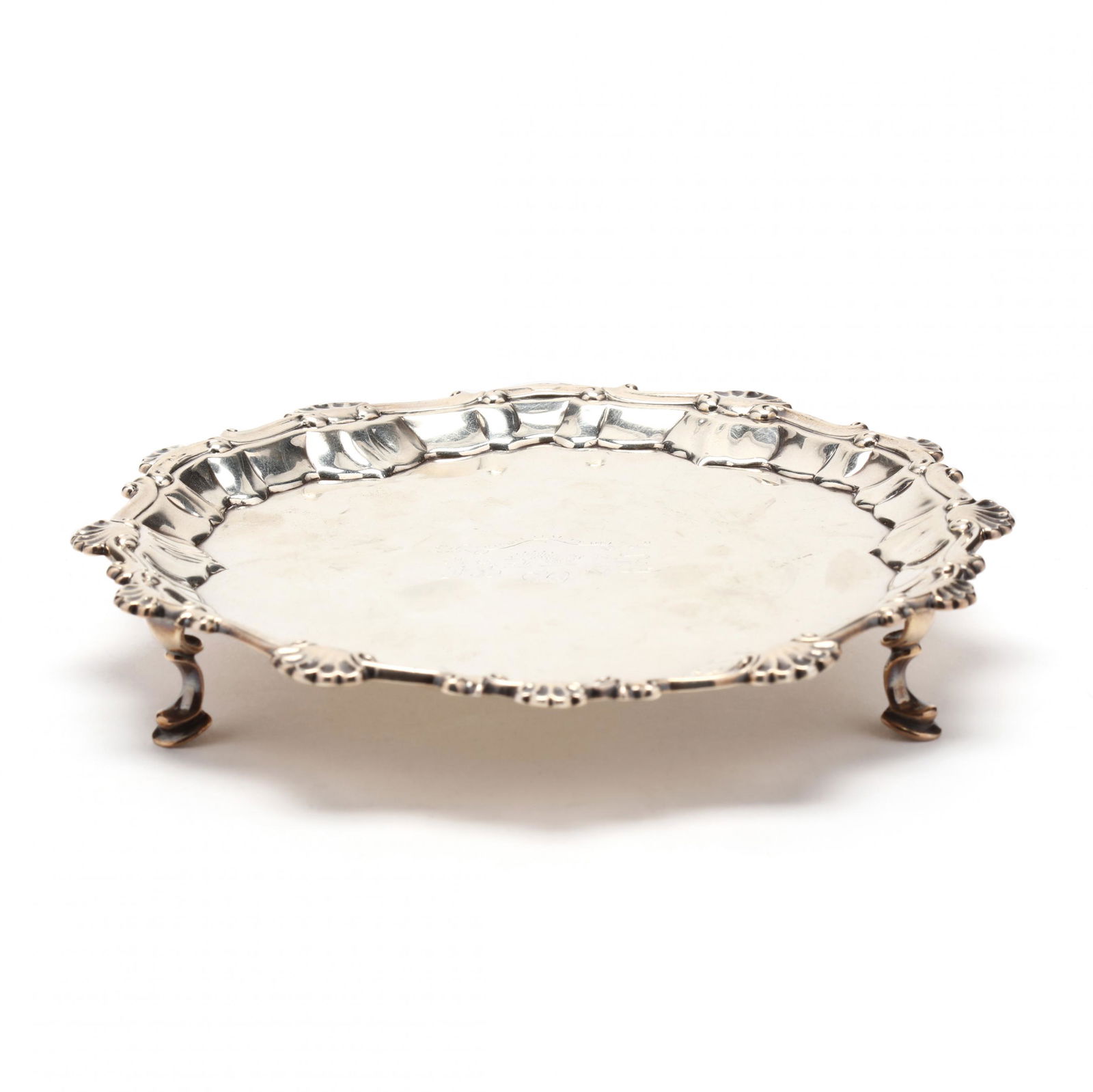 An Early George III Silver Salver: An Early George III Silver Salvermark of Ebenezer Coker, London (1761), border in the Rococo style with shells and scrolls, raised on three hoof feet, central armorial engraving of the period and feat