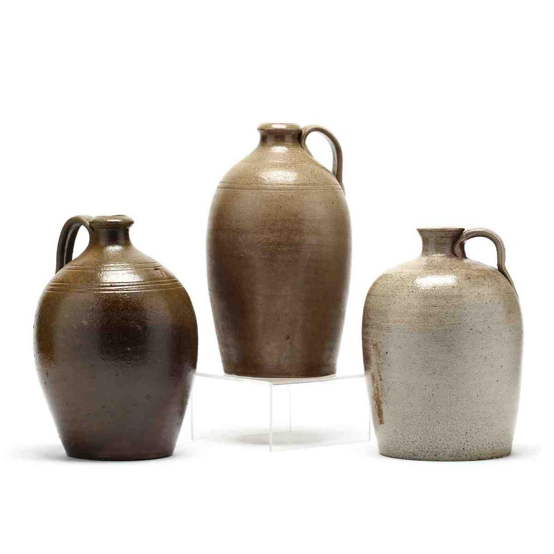 Three NC Pottery Jugs: Three NC Pottery Jugs19th century, salt-glazed stoneware, a one gallon jug so stamped with two bands of tooling to the shoulder (base chip); a one gallon jug with grooved handle, flat rim (flea bit at