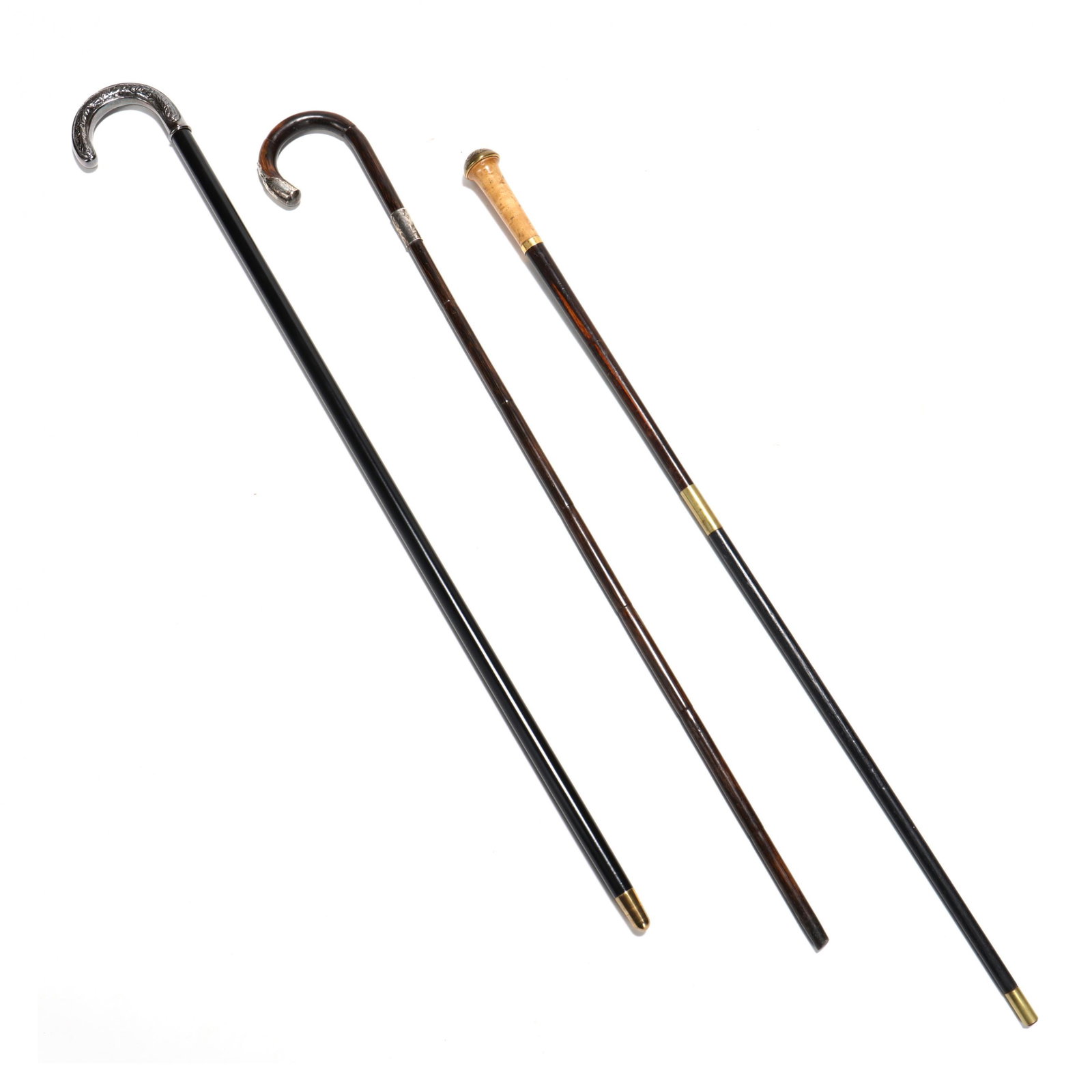 Three Vintage Canes: Three Vintage Canes including a bent bamboo cane with sterling silver mounts; an ebonized wood cane with silverplate handle; and a wood specimen stick with chased brass cap. 36 in. Private Collection,