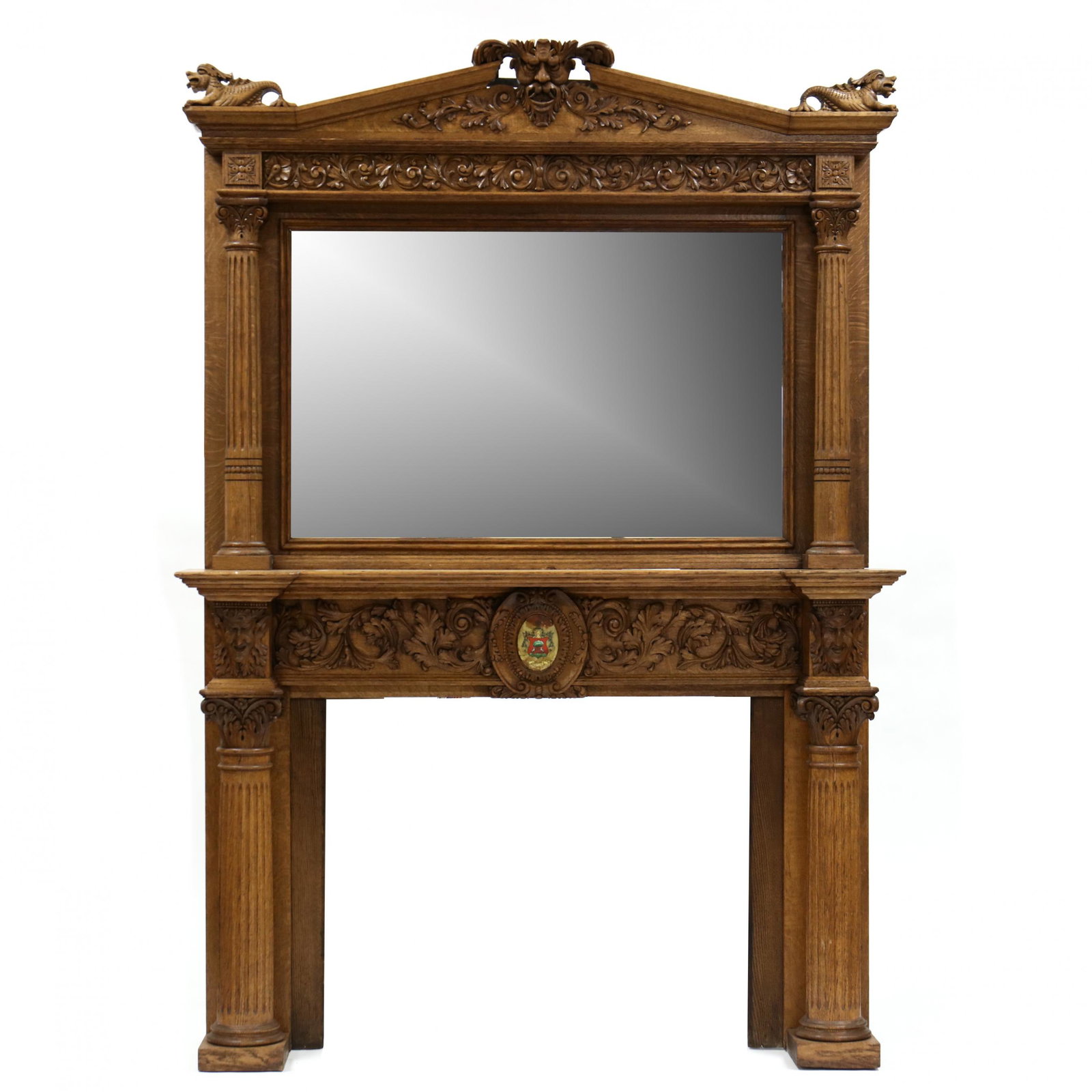 Large Antique Carved Oak and Mirrored Mantel: Large Antique Carved Oak and Mirrored Mantel late 19th century, two part form, relief carved arched pediment with central mask flanked by dolphins, rectangular mirror with fluted column supports and r