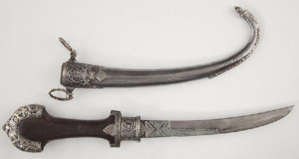 Middle Eastern Jambiya Dagger: Middle Eastern Jambiya Dagger wooden grip with ornate silver mounts, silver geometric inlays on curved steel blade, silver sheath embellished with applied scrolled throat and engraved finial. 16.5 in.