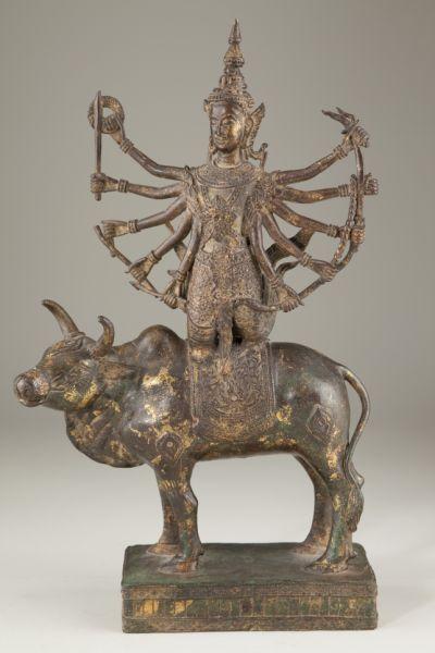 Thai Gilt Bronze Shiva on Bull: Thai Gilt Bronze Shiva on Bull cast bronze with gilt and verdigris highlights, the ten- armed Hindu goddess depicted kneeling on the bull. 16.5 in. One weapon broken.