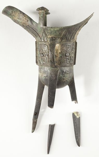 Chinese Bronze Libation Bowl: Chinese Bronze Libation Bowl Han or Chou dynasty, inverted helmet shaped with conventional archaic pattern, one ring handle, tripod tapered legs. 8.25 x 5.75 in.