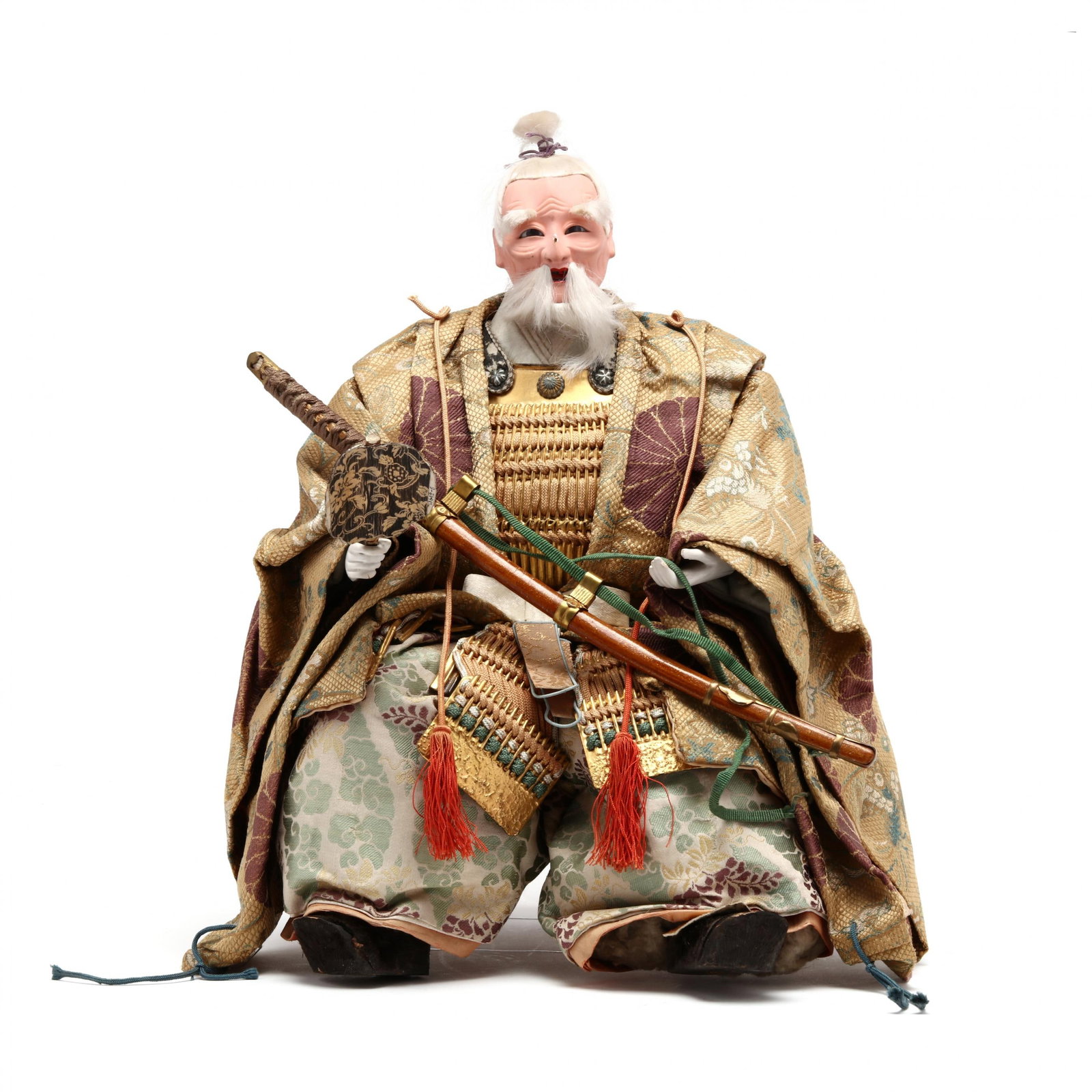 A Japanese Musha Nignyo Doll: A Japanese Musha Nignyo Dolllate 19th century, hand-painted plaster with applied hair, finely crafted in an ornate costume with silk textiles and woven gold-toned armor, seated yielding a sword in one