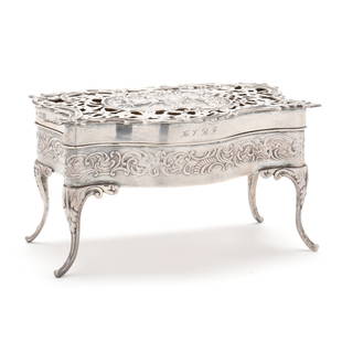 An Edwardian Silver Dresser Box, Mark of William Comyns & Sons: An Edwardian Silver Dresser Box, Mark of William Comyns & Sons London (1909), base with scrolled foliate repousse, reticulated hinged lid with figural scene within a cartouche opens to reveal a gold