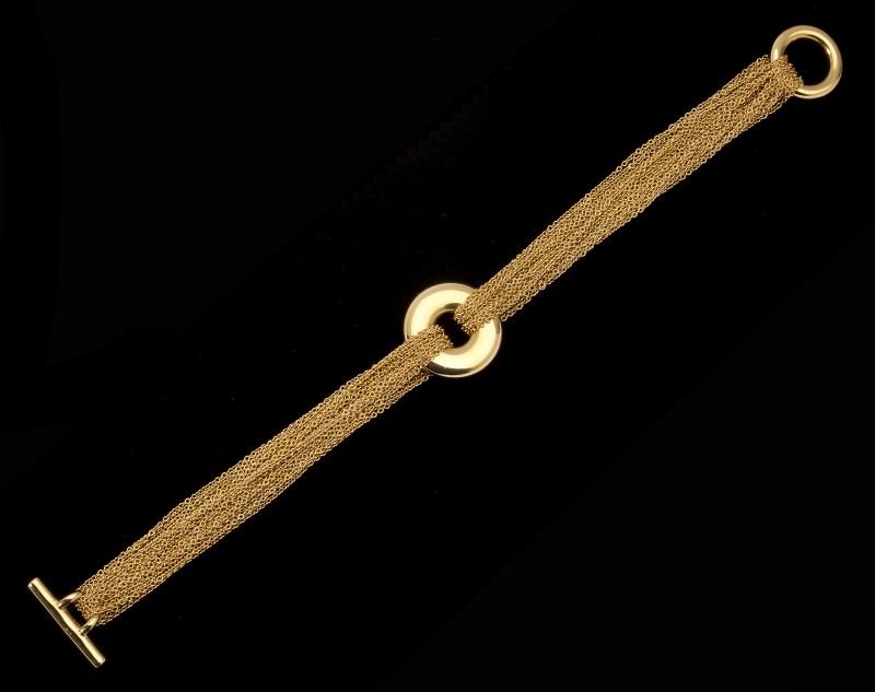 Gold Multi-Chain Bracelet, Tiffany & Co.: Gold Multi-Chain Bracelet, Tiffany & Co. composed of (12) fine link trace yellow gold chains joined to a central open circle terminating in a toggle clasp, with maker's mark and stamped 750. Accompani