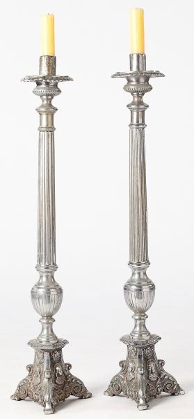 Pair of Continental Altar Candlesticks: Pair of Continental Altar Candlesticks19th century, silvered metal, with candle socket above broad scalloped drip pan surmounting fluted column and urn standard, trifid base with relief design featuri