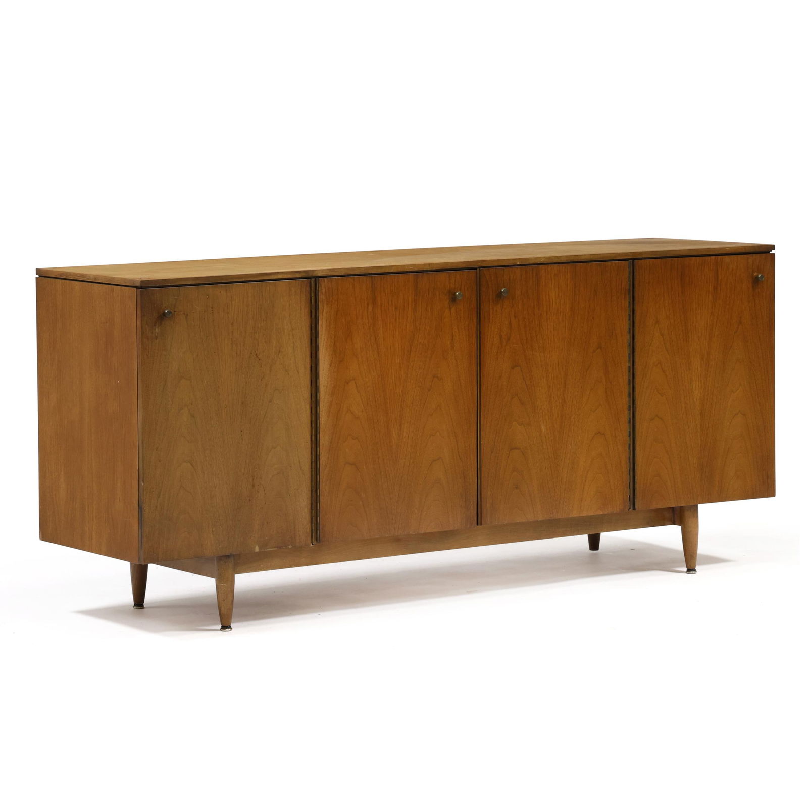 John Stewart, Mid-Century Walnut Credenza: John Stewart, Mid-Century Walnut Credenza circa 1960, walnut veneer, four hinged doors, divided interior with three fitted drawers and two shelves, turned tapered legs, labeled. 32 x 72 x 19 in. 
