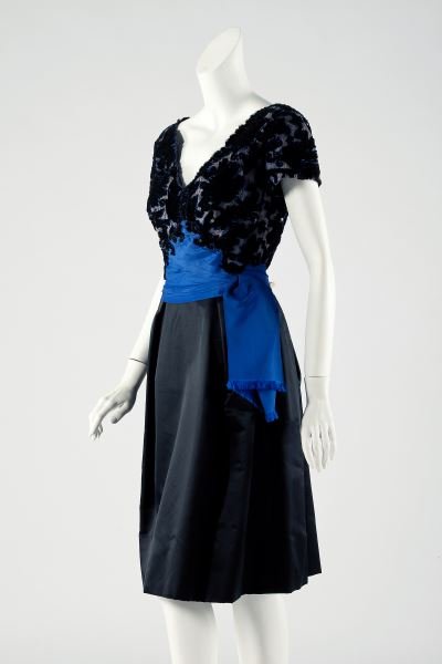 Satin and Velvet Cocktail Dress, Oleg Cassini: Satin and Velvet Cocktail Dress, Oleg Cassini circa 1954-1955, designed as a cut velvet and netted top on a linen ground, the waist accented by a bright blue satin ribbon which drapes asymmetrically t