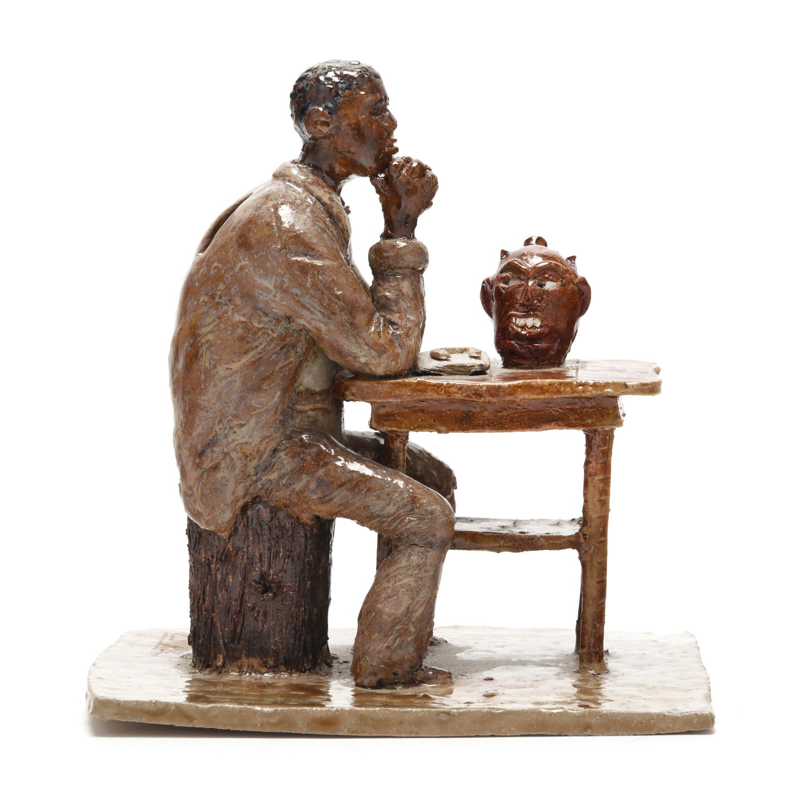 Southern Pottery Figural of Seated Man and Face Jug, Signed EB: Southern Pottery Figural of Seated Man and Face Jug, Signed EBlate 20th century, glazed figurine featuring a man seated on a stump with arms resting in prayer, on a table with a horseshoe and face jug