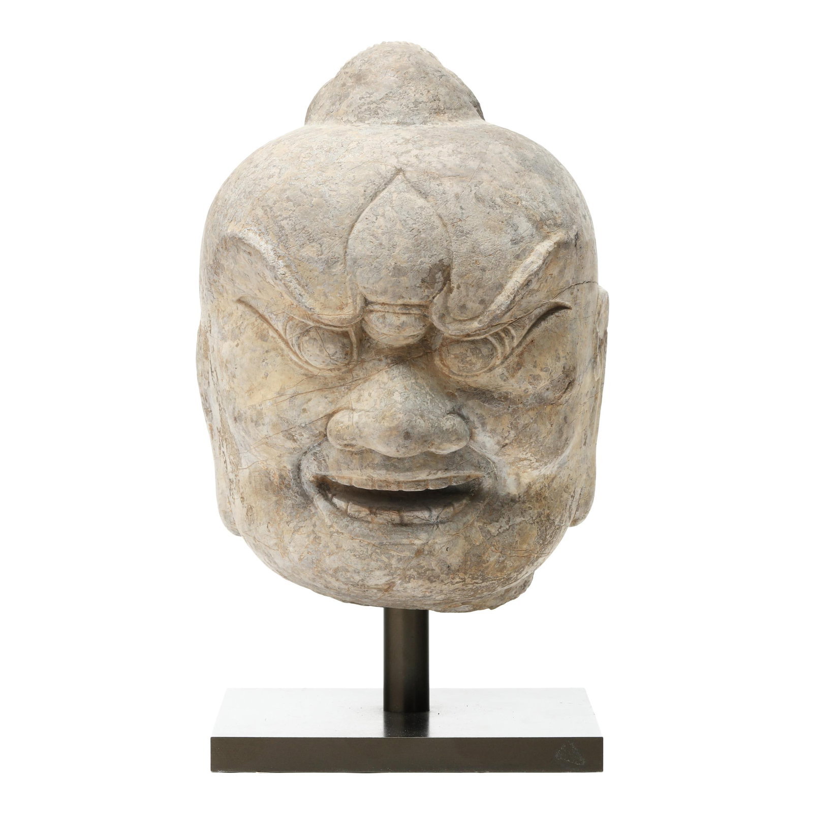 A Chinese Carved Stone Head of a Guardian Figure: A Chinese Carved Stone Head of a Guardian Figure Tang dynasty (618-907), carved with a powerful fierce expression, bulging eyes beneath sharply arched brows, a broad nose, and an open mouth revealing 
