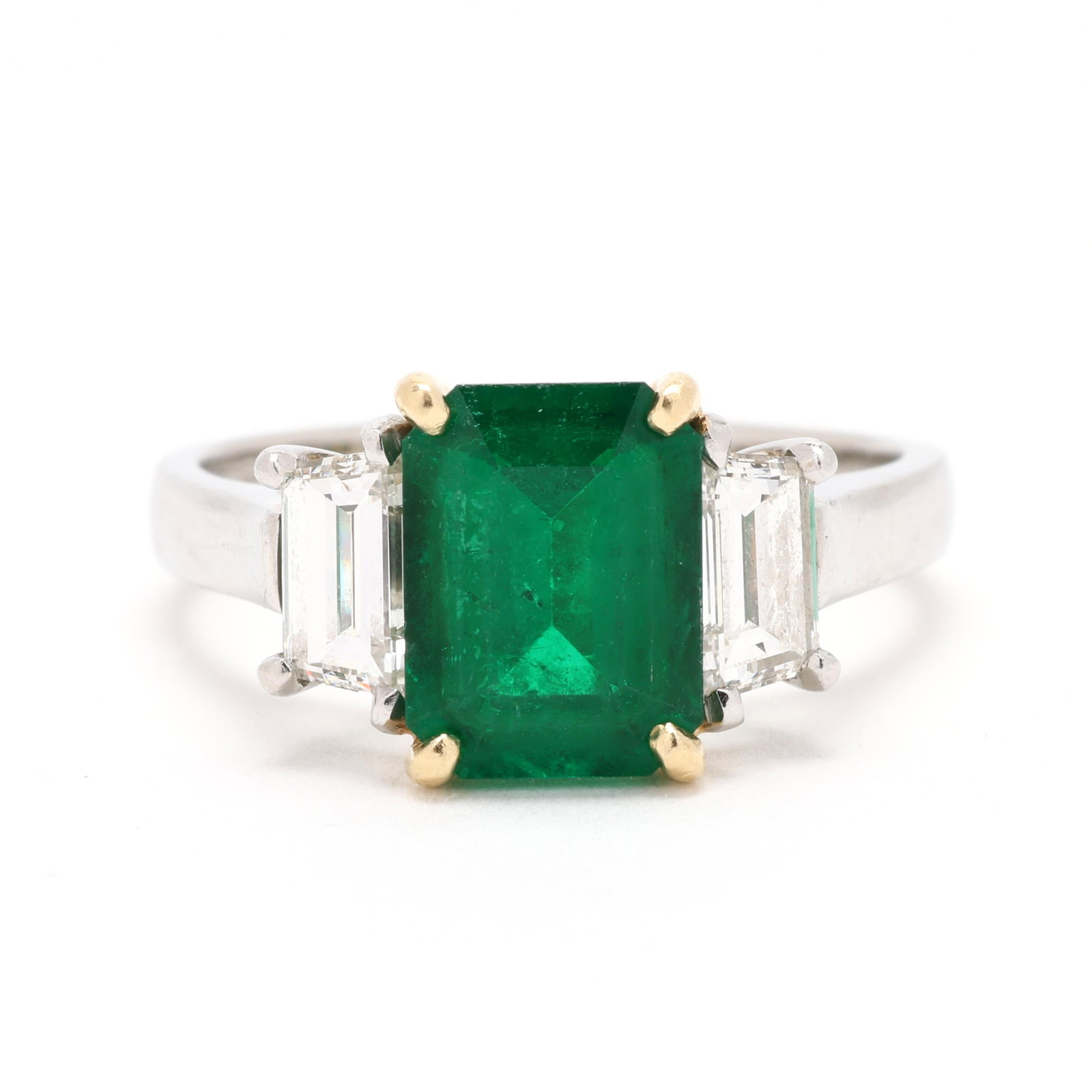 Platinum, Gold, Emerald, and Diamond Ring: Platinum, Gold, Emerald, and Diamond Ring set to the center with an emerald cut emerald (9.5 x 7.2 x 4.4mm) weighing approximately 2.20 carats and prong set in gold, set to each side with a trapezoid 