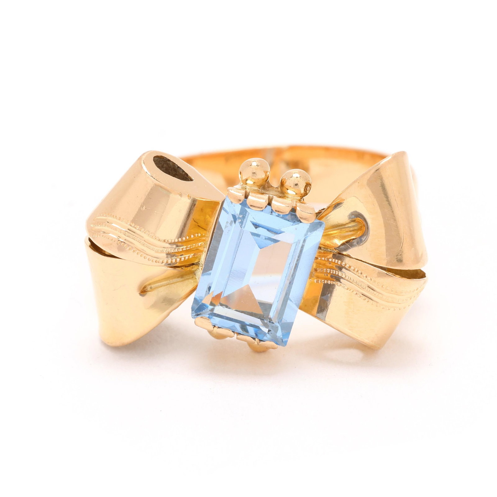 Retro Gold and Blue Spinel Ring: Retro Gold and Blue Spinel Ring the ring in the form of a bow, centered on an emerald cut blue spinel (8.1 x 6.0mm), stamped 750. 12 x 20mm; Ring size 6 3.1 dwt. Spinel displays a very slightly