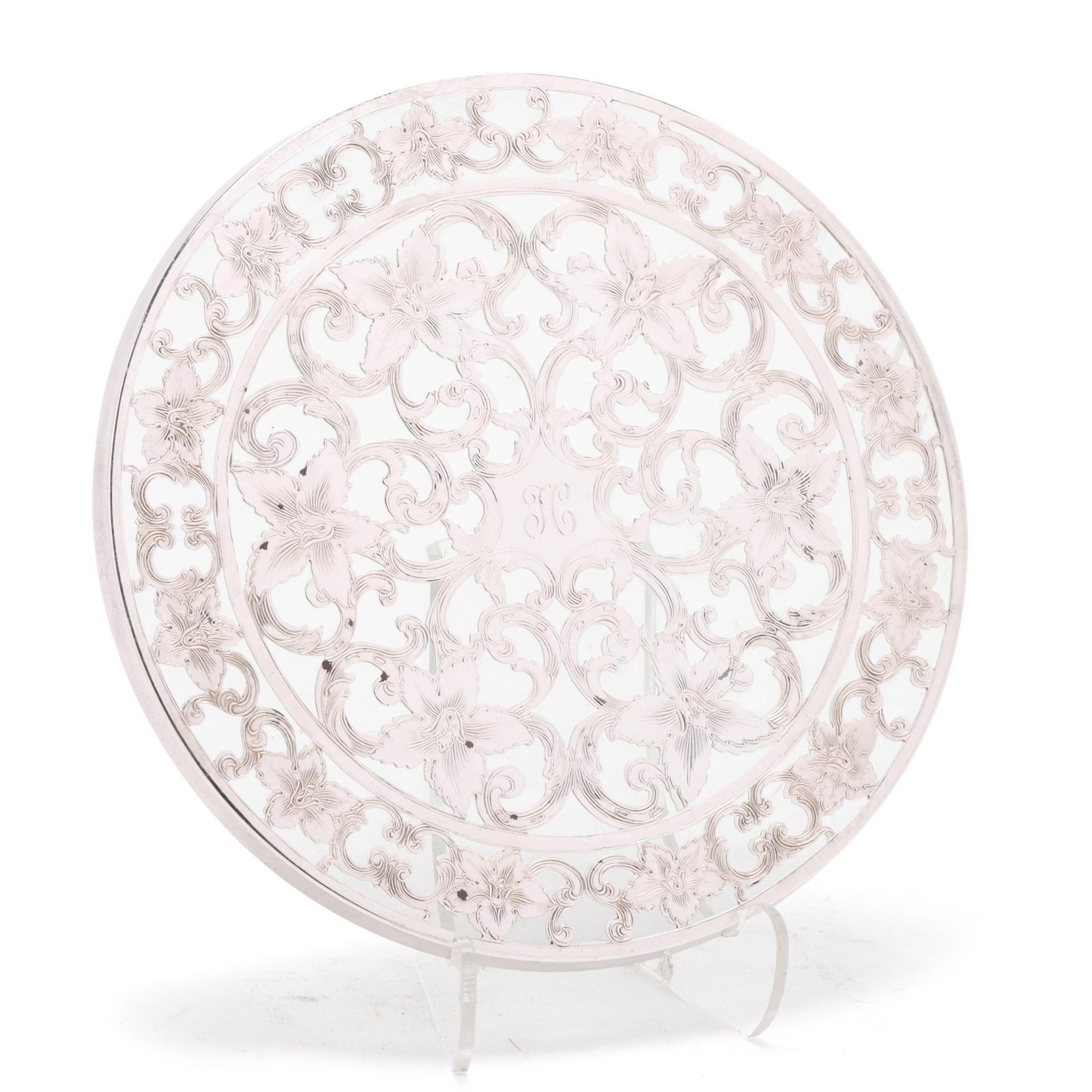 Sterling Silver Overlaid Trivet by Webster: Sterling Silver Overlaid Trivet by Webster 20th century, the glass trivet with openwork floral and scrolled overlay, featuring an "H" monogram to the center. 6 in. dia. From the Collection of Joseph a