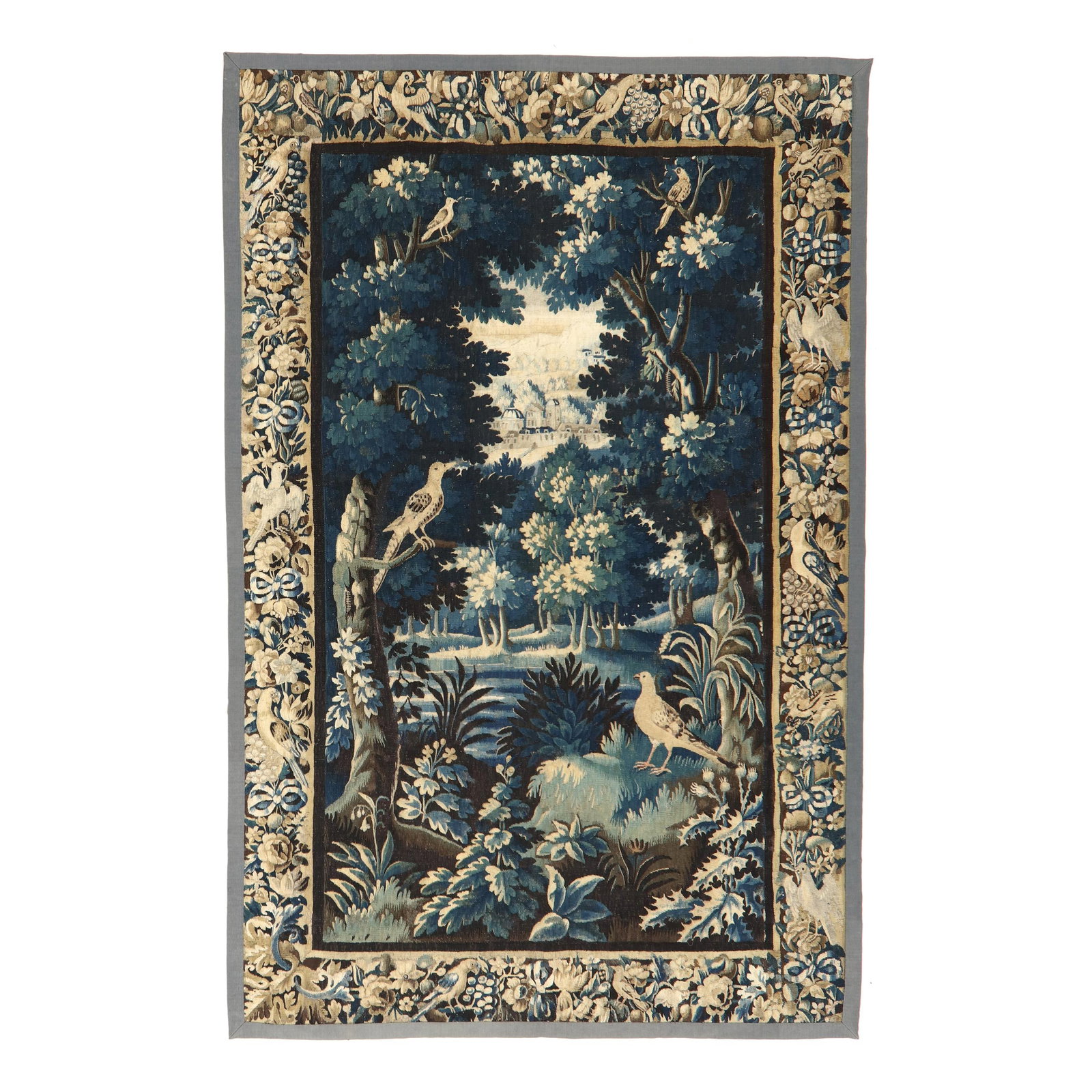 Antique Flemish Verdure Tapestry: Antique Flemish Verdure Tapestry 18th century or earlier, wool and silk, depicting a verdant landscape with trees and birds, architecture in the distance, the border with beribboned floral clusters