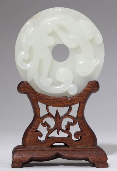 Chinese Qing Dynasty White Jade Bi Disc: Chinese Qing Dynasty White Jade Bi Disc possibly 18th century, carved with a high relief chilong crawling over the face and repetitive dots on the back, displayed on a custom wooden stand. 2 3/8 in. d