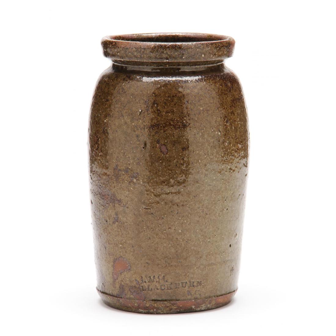 NC Pottery Preserve Jar, John Wesley Hilton (Catawba: cylindrical in form with high mouth and interior rim, light olive alkaline glaze with numerous tiny quartz inclusions, impressed stamp near base "JWH Blackburn." 8.75 in. Described in "The Potters of