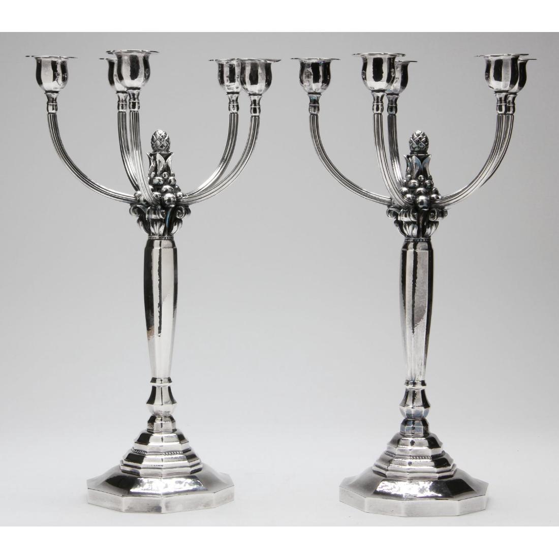 Pair of Georg Jensen Sterling Silver Candelabra: designed by Johan Rohde, pattern number 474, with post 1945 hallmark and Rohde's designer mark, the domed and faceted foot supporting a conforming standard terminating in a berry and foliate scroll gr