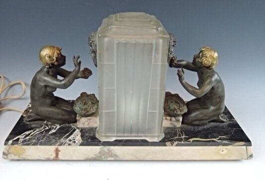 SABINO ART DECO FIGURAL LAMP: Signed Sabino Art Deco Figural Lamp! Wonderful C.1920’s Art Deco Lamp with 2 figures facing the center shade signed Sabino. On each side of the shade is a metal mask. 15 1/2 wide by 8 1/2 tall. Moun