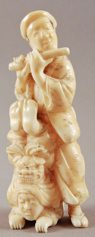 Carved Asian Ivory Musician & Clown: Carved Hippo or Whalebone Ivory Musician & Clown. The figure depicts a man playing the flute with a man resting on his hands with feet up with a foo dog headdress. Unsigned. In good condition. Measure