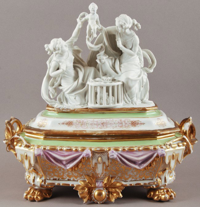 Old Paris Porcelain Covered Box with Figural Group: French 19C Old Paris type covered box with gilt decoration and drapery that ends in paw feet. The top is porcelain with a parian figural group of two women with a baby aloft in their arms, with anothe