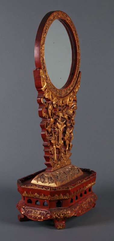 Ornate Gilt Carved Table Screen Mirror: Carved gilt 19th C Chinese Table Mirror. This carved 19th C gilt and red lacquered table mirror has a carved central support with Chinese immortals and floral carved base and frame. The mirror is in g