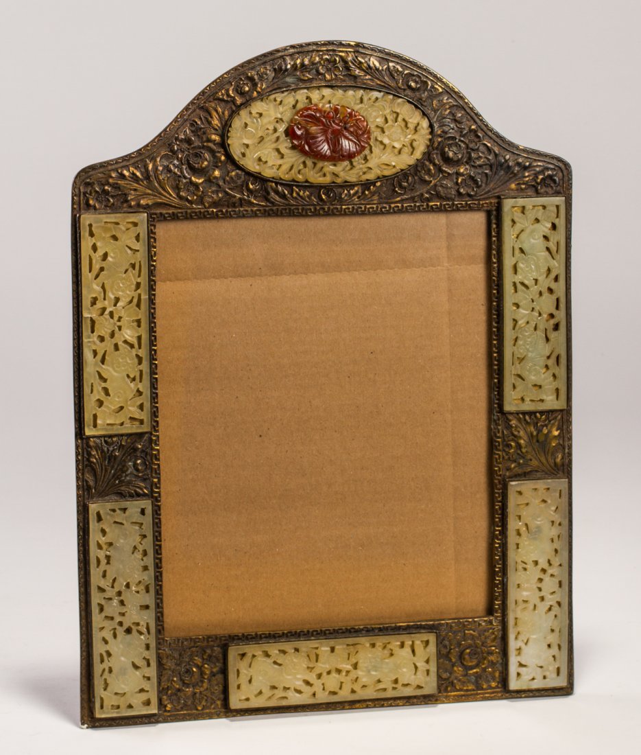 Art Deco Chinese Soapstone Easelback Picture Frame: Art Deco Carved Chinese Soapstone and Carnelian Easelback Picture Frame. The ornate metal floral embossed brass plated picture frame has panels of carved soap stone with an applied oval carnelian carv