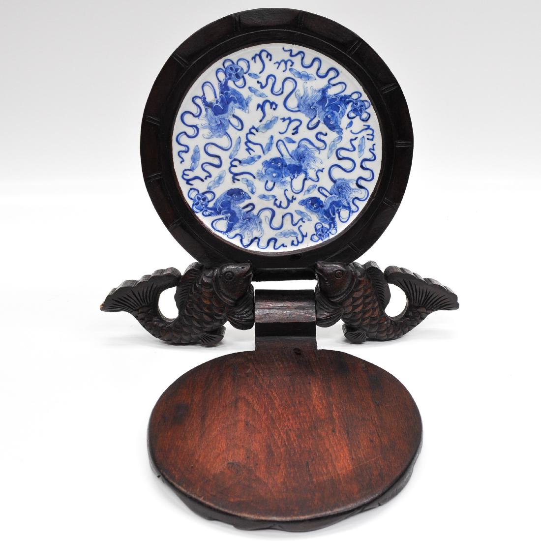 A Chinese Carved Wood Sculpture with Tile: Depicting fish with flower opening to show a blue and white decor tile depicting temple lions, sculpture measures 32 x 28 cm.