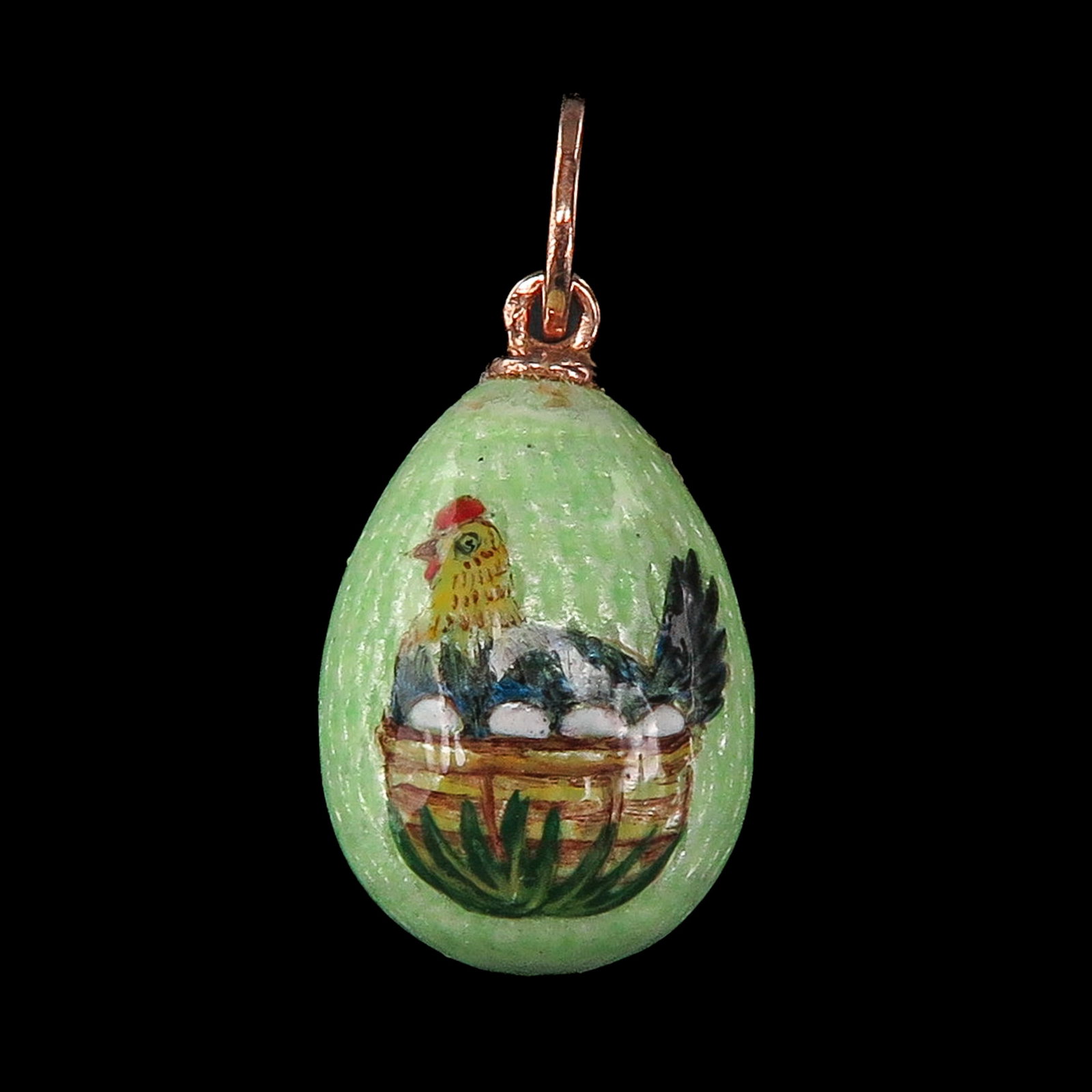 An Enamel Pendant: Enameled, in the shape of an egg, with a chicken sitting on a basket, with gold mountings, length 18 mm.