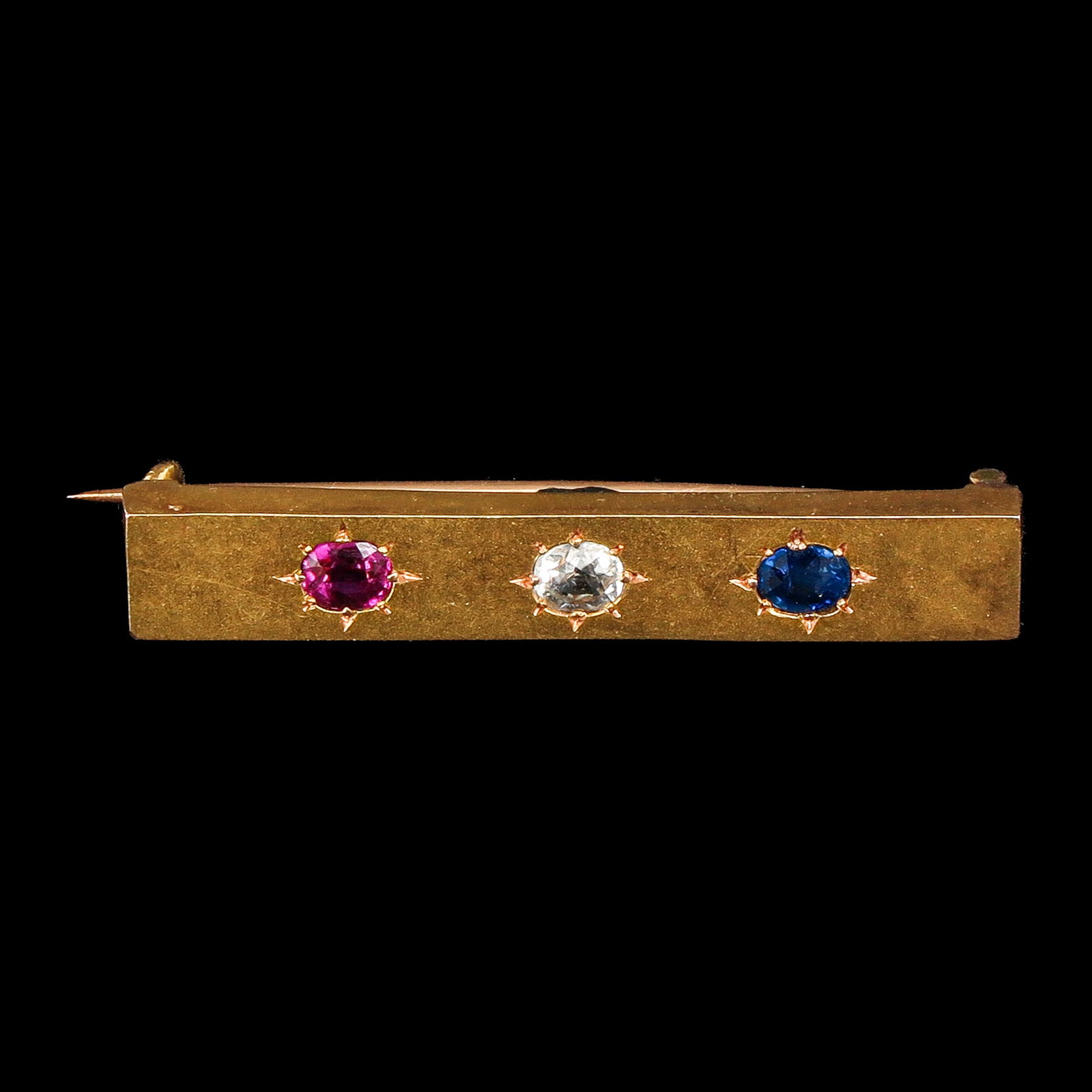 A Gold Bar Pin: Gold, set with diamonds, rubies, and sapphires in star-shaped settings, length 40 mm