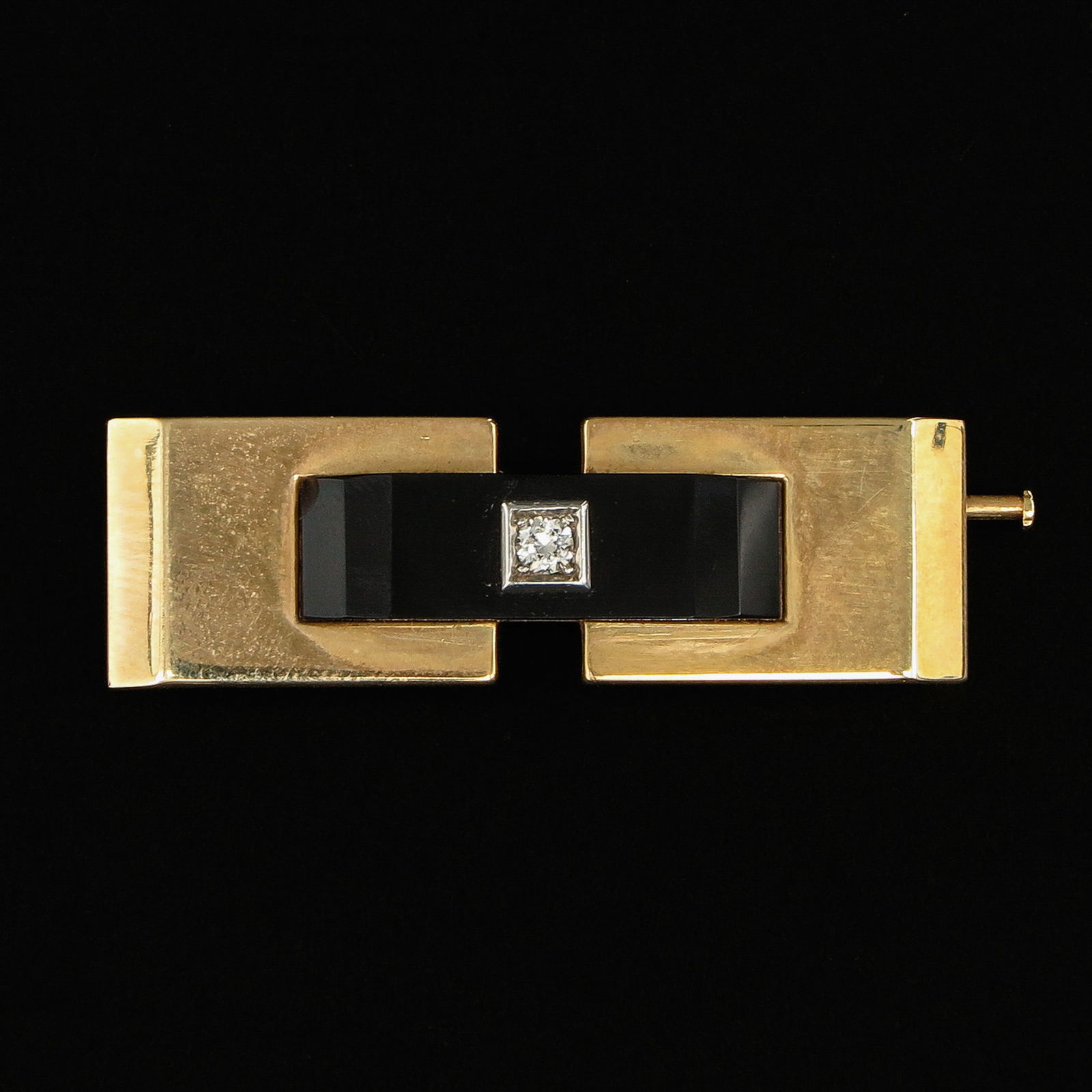 An Art Deco Brooch Set with Diamond: Art Deco period, 14-karat gold, set with onyx and a central diamond, length 41 mm.