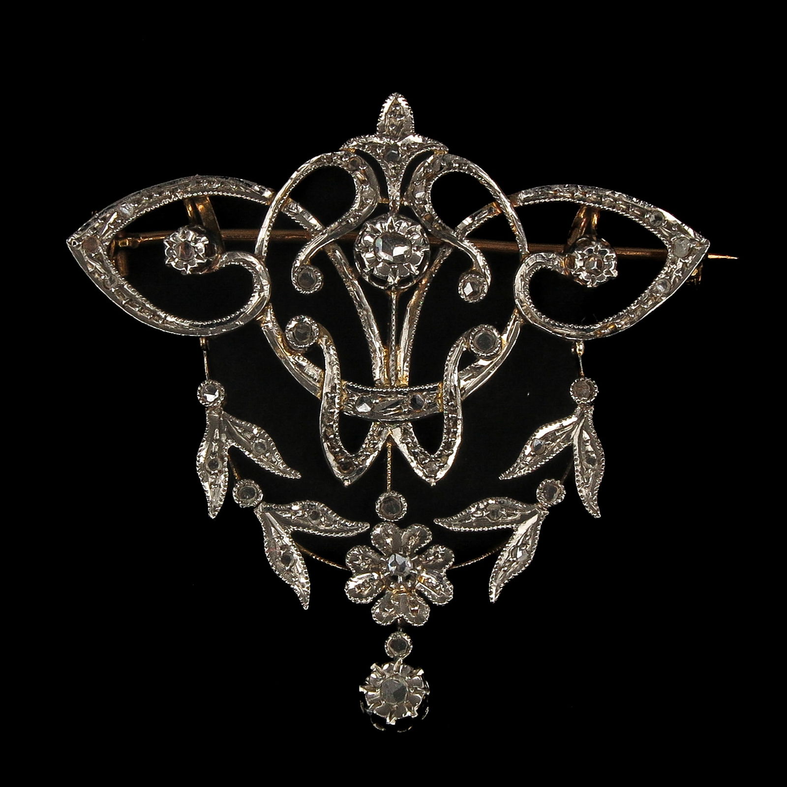 An Art Nouveau Diamond Brooch: Art Nouveau / Belle Époque, ca. 1900, silver and gold, featuring an openwork scroll and floral motif, set with rose-cut diamonds, 45 x 45 mm.
