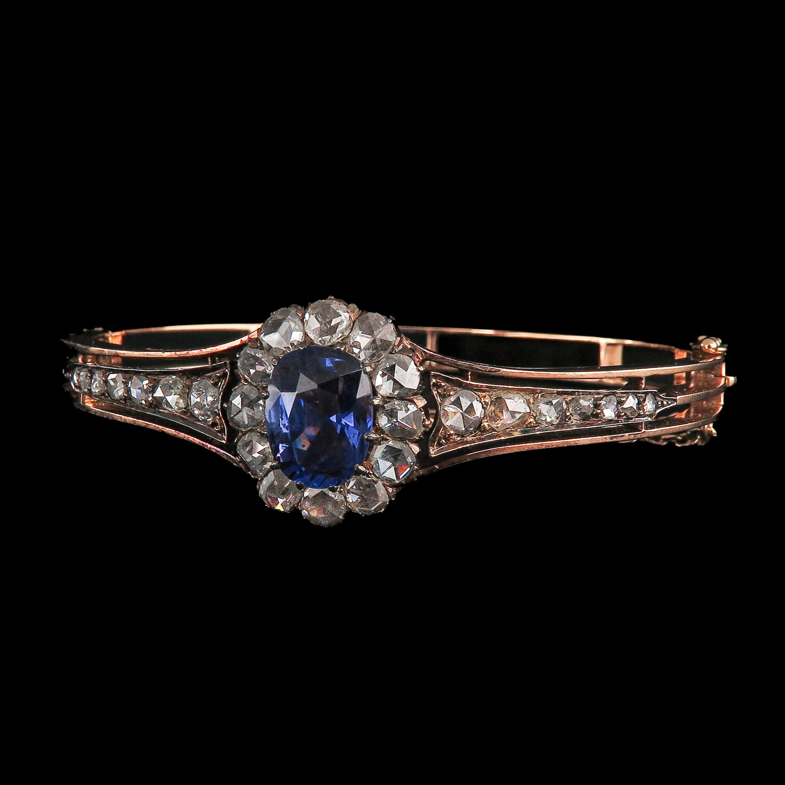 A Sapphire and Diamond Bracelet: 18 Krt. gold, set with an oval-cut Ceylon sapphire of approx. 4 ct., surrounded by 12 brilliant-cut diamonds and set on either side with another approx. 14 brilliant-cut diamonds, inner diameter 6.5 c