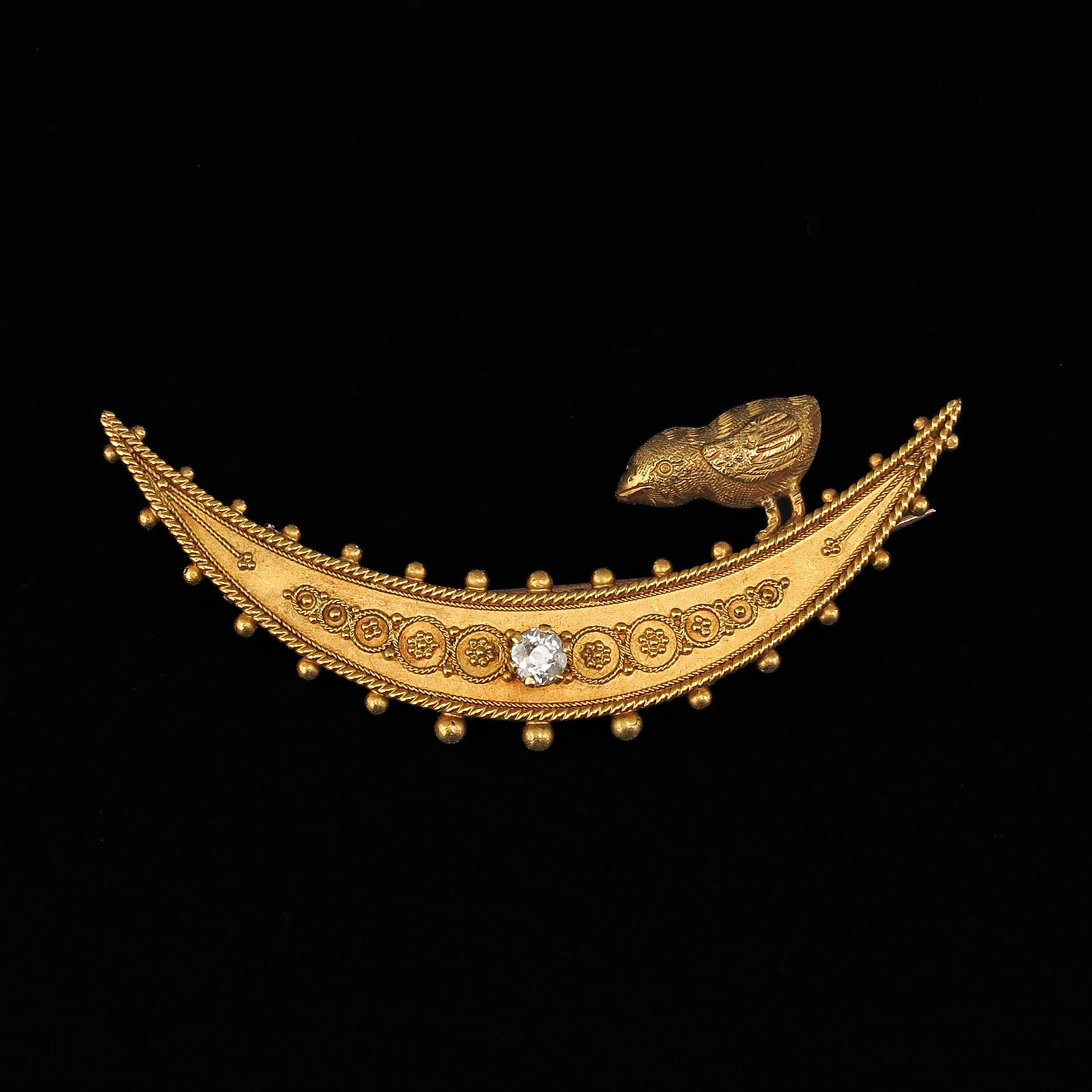 A 14KG Diamond Brooch: 14 Krt. gold, in the shape of a crescent moon, with a central diamond and a small bird sitting on the side, length 49 mm
