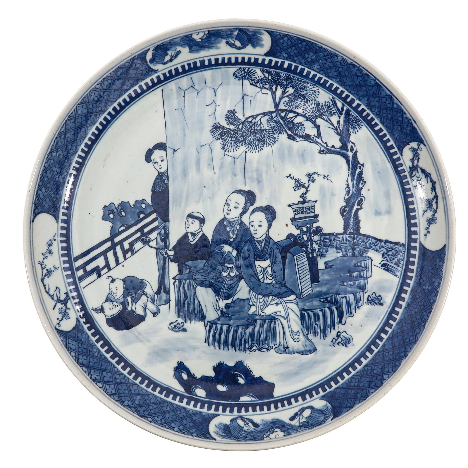 A Blue and White Plate: Decorated with a garden scene with elegant ladies, attendants and children beneath a tree, within a geometric border, Kangxi mark, 40 cm in diameter, hairline.
