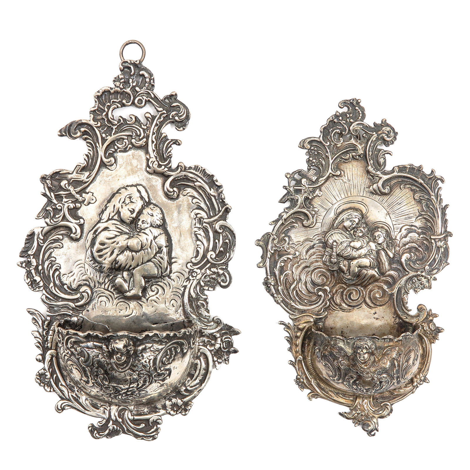 A Lot of 2 Silver Holy Water Fonts: of 2 silver holy water vessels, richly decorated with repoussé, one with a depiction of Mary with Child, the other with a Pietà, height 20 cm.