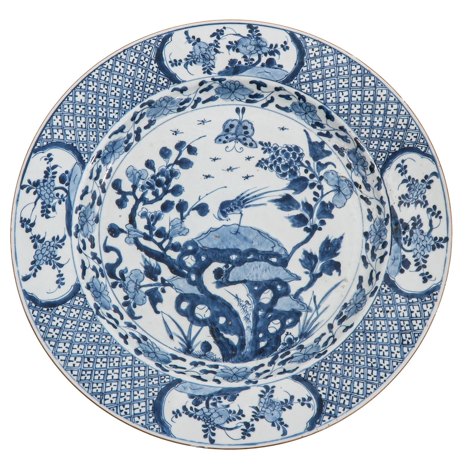 A Blue and White Charger: Decorated with a bird perched on a pierced rockwork amidst flowering branches, the border with floral cartouches on a diaper ground, 18th Century, 39 cm. in diameter, hairline.