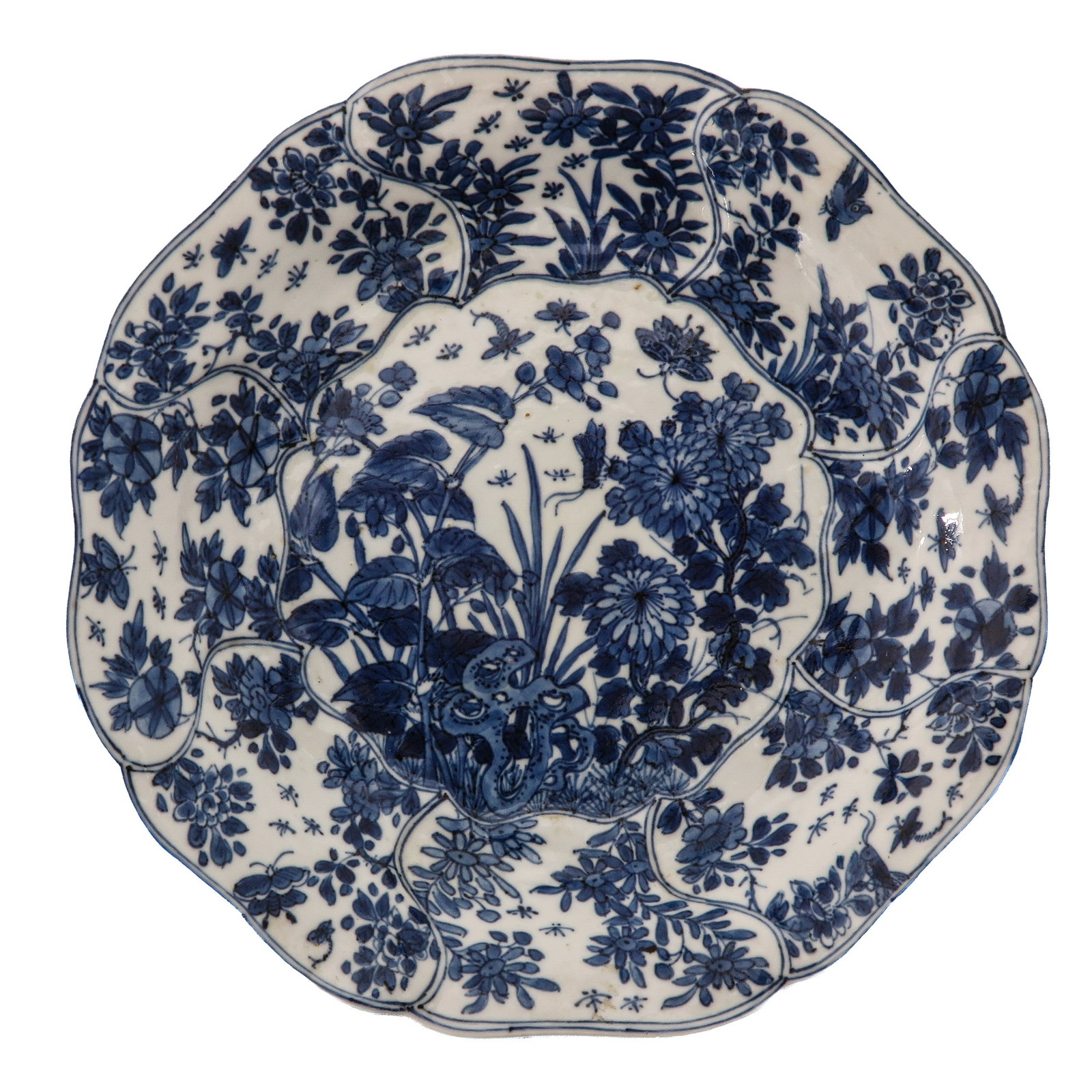 A Blue and White Lotus Shape Plate: With lobed rim, densely decorated with flowering plants, foliage and butterflies surrounding a central floral garden scene, 18th Century, 21 cm. in diameter.
