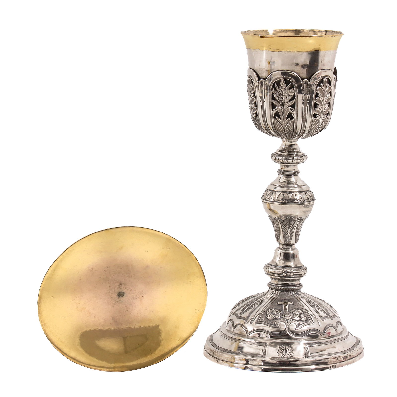 A Chalice: silver, with paten, hallmarked with Dutch eagle mark, richly decorated with floral motifs, provided with a cross on the foot and a partly gilt cuppa, height 25 cm.