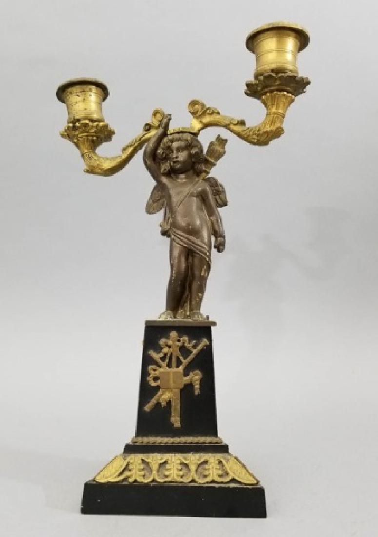 Antique Bronze & Ormolu Cupid Motif Candelabra: Antique Bronze & Ormolu Cupid Motif Candelabra. Neo Classical design motif at base incorporating a statue of Cupid with his arrows on his back. Measures 12 inches in height.
