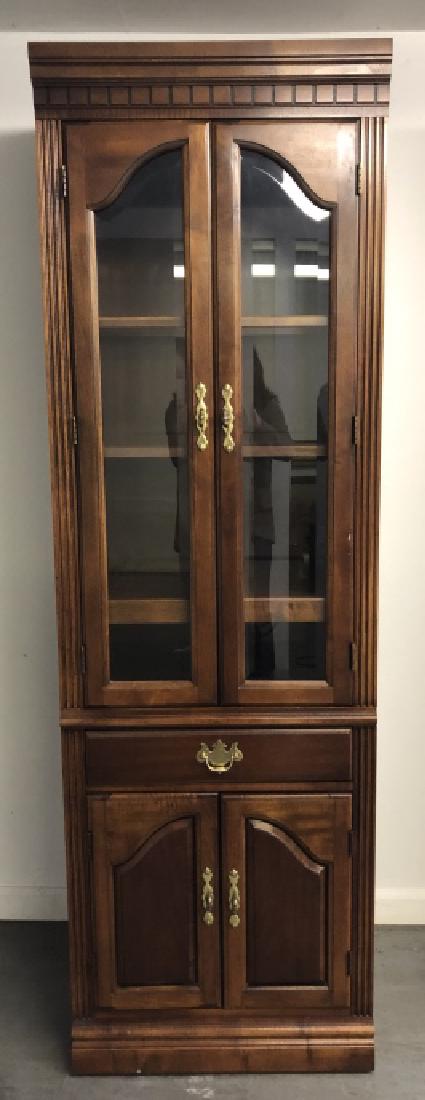 Sheraton Style Lit & Glass Front Curio Cabinet: Sheraton Style Lit & Glass Front Curio Cabinet. Features a carved pediment, glass front cabinet with interior shelving, lighting, one pull out drawer and a lower cabinet. 77 inches x 24 inches x 18 in