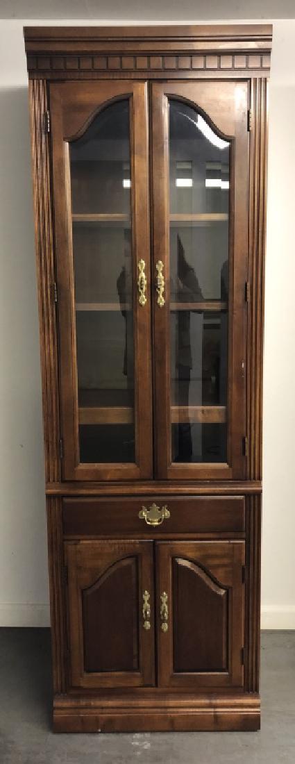 Sheraton Style Lit & Glass Front Curio Cabinet: Sheraton Style Lit & Glass Front Curio Cabinet. Features a carved pediment, glass front cabinet with interior shelving, lighting, one pull out drawer and a lower cabinet. 77 inches x 24 inches x 18 in