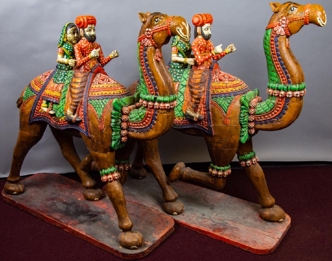 Pair Hand Carved Indo Camel with Riders Sculptures: Pair Hand Carved Indo Camel with Riders Sculptures. Pair of hand carved and hand painted large carvings of camels each with a male and female rider dressed in Indian style clothing. 34 inches x 32 inc