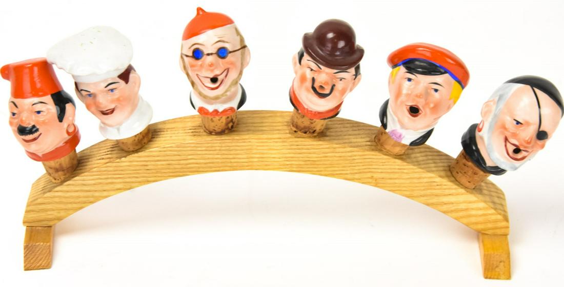 German Porcelain Wine Cork Figure Heads on Rack: German Porcelain Wine Cork Figure Heads on Rack. Vintage German Porcelain figural heads made into wine corks with a wooden rack in which they all fit. Rack is 11 inches long.