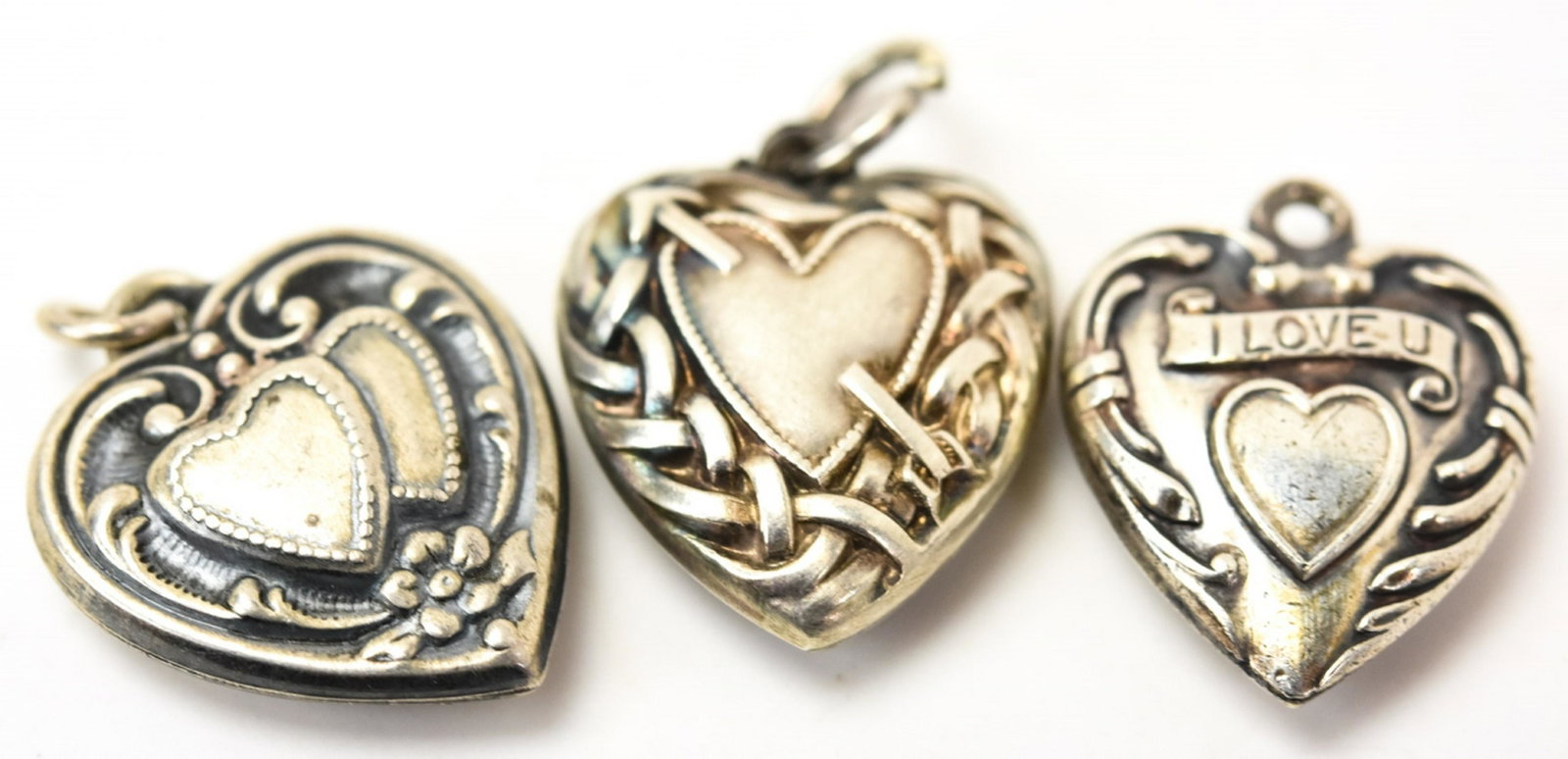 Three Vintage Sterling Silver Puffy Heart Charms: Three Vintage Sterling Silver Puffy Heart Charms. Each with a heart design at center. Double heart w flowers measures 5/8ths of an inch in length w bail.
