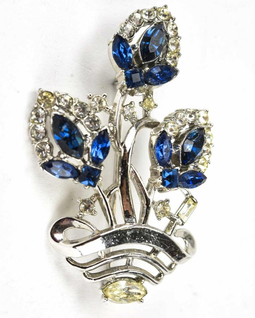 Trifari C 1952 Rhinestone Floral Motif Brooch: Trifari C 1952 Rhinestone Floral Motif Brooch. Motif of flowers in a vase with blue and clear rhinestones by Trifari. Measures 2 inches x 1.25 inches.